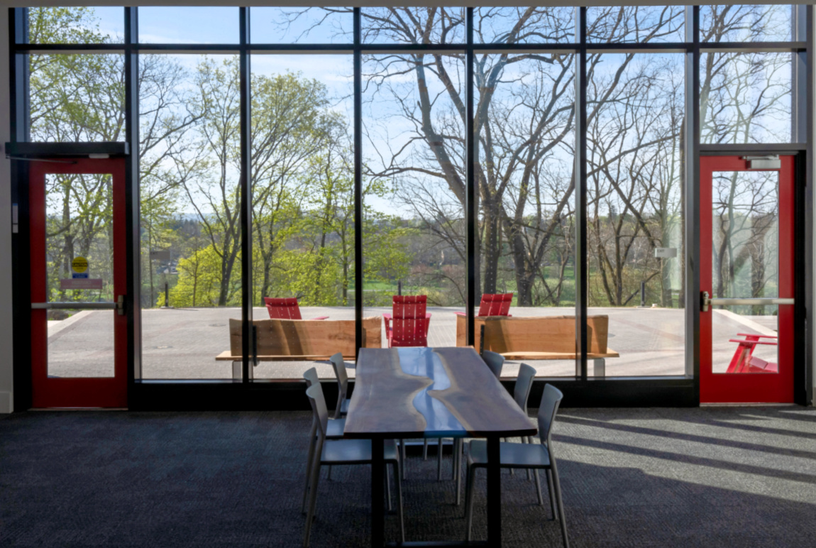 A view of an outside terrace with large windows, benches and red chairs.